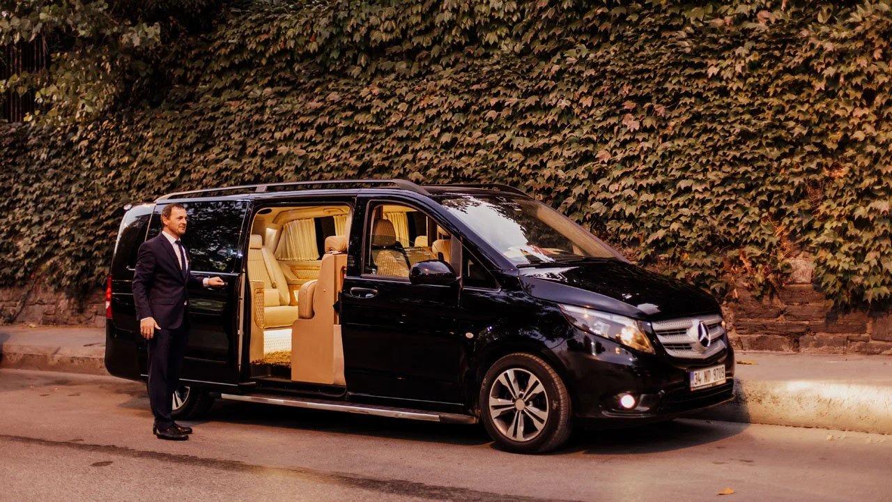 A private chauffeur holding open the door of a Mercedes van used for clinic transfers