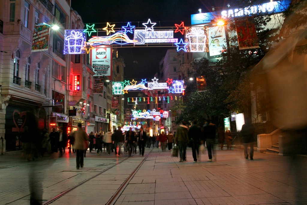 İstiklal Avenue at night, busy and well-lit, where the bar-invitation scam is aimed at walkers rather than the street itself being unsafe